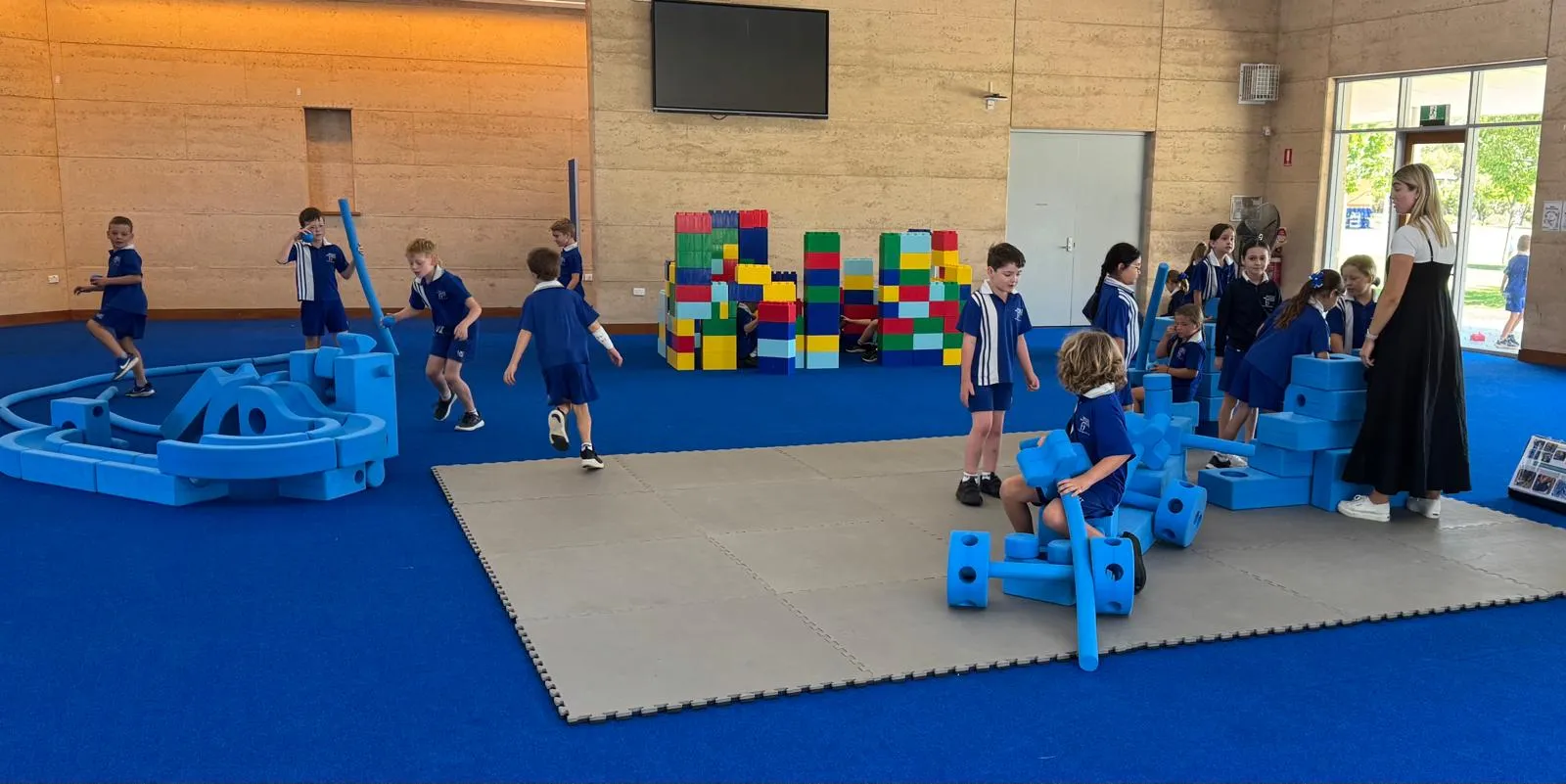 Primary school students in uniform playing with blue foam blocks and giant building bricks in a school hall