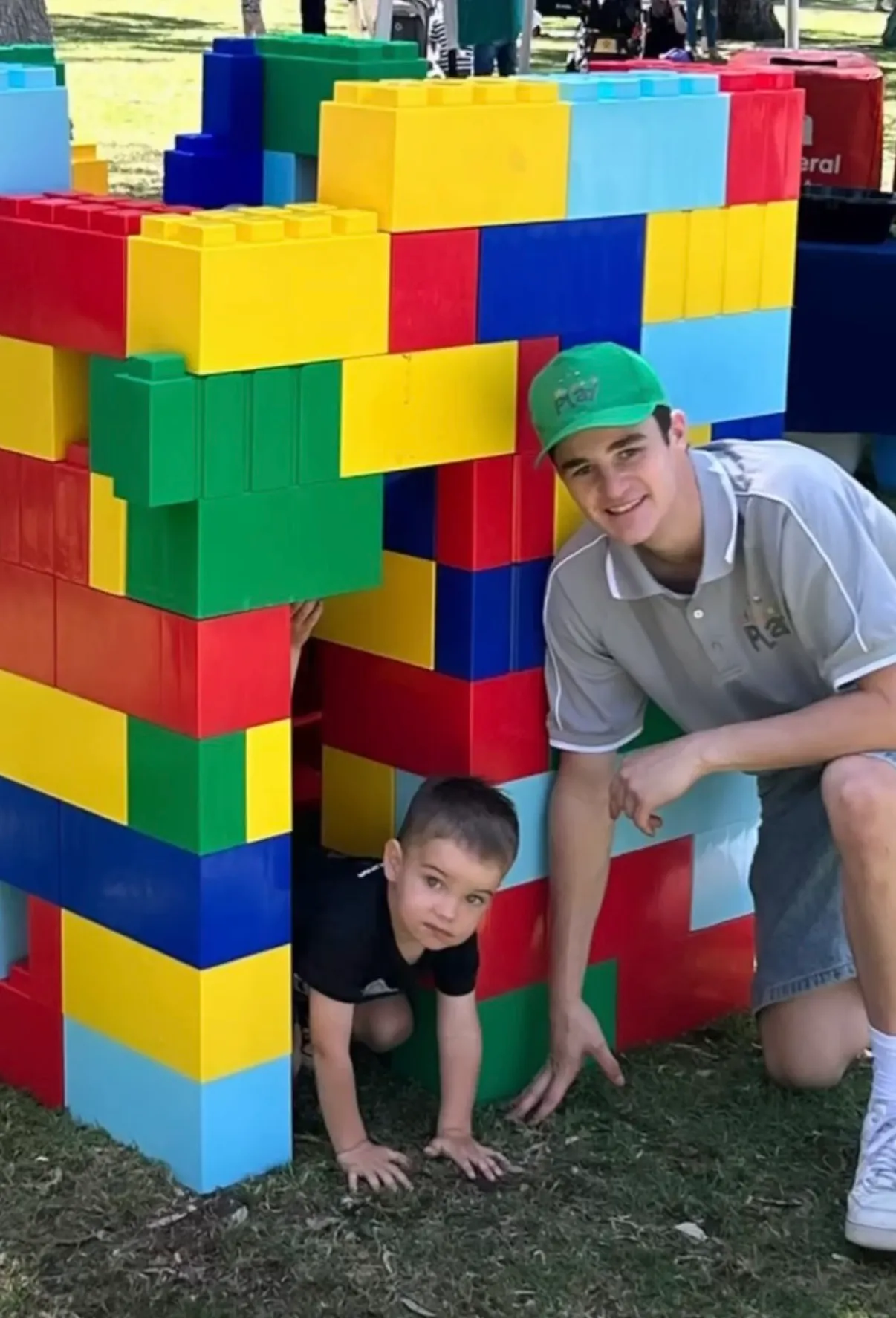 Kieran crouching beside a wall of giant Lego bricks with a child